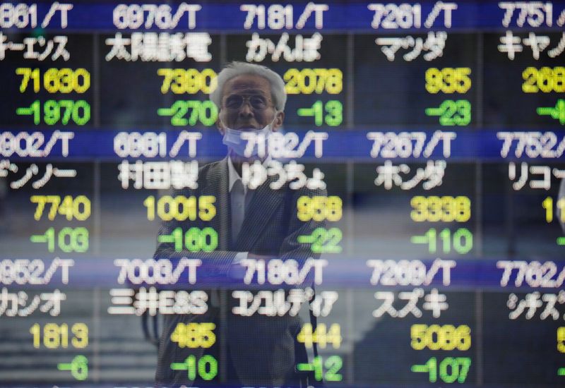 FILE PHOTO: A man wearing a protective mask, amid the COVID-19 outbreak, is reflected on an electronic board displaying stock prices outside a brokerage in Tokyo