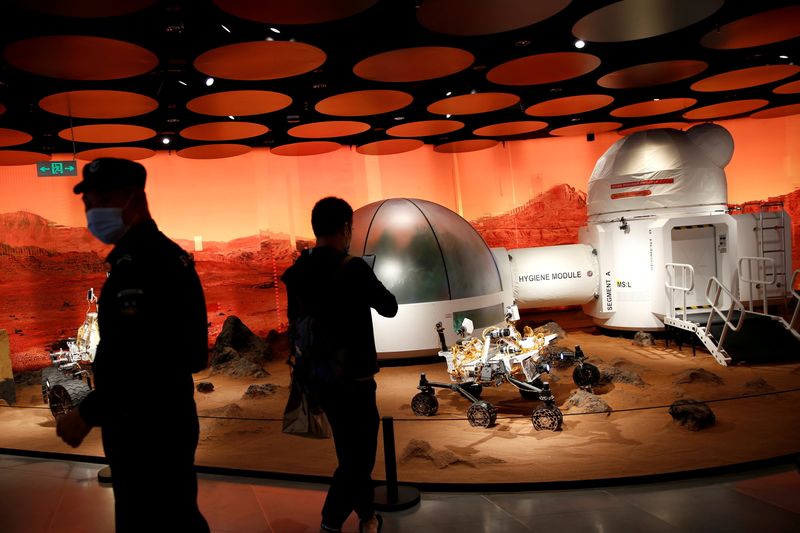 FILE PHOTO: People wearing face masks following the COVID-19 outbreak are seen near models of a Mars base and a rover displayed inside the SKP-S shopping mall in Beijing