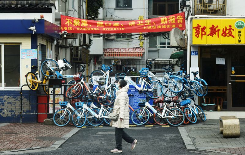 Woman wearing a face mask walks past an entrance to a residential compound that has been blocked by shared bicycles, as the country is hit by an outbreak of the novel coronavirus, in Hangzhou