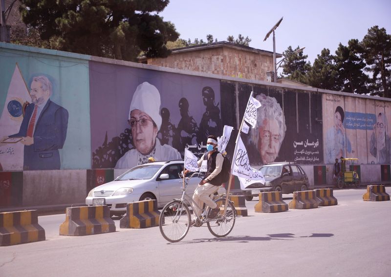 An Afghan man rides on his bicycle as he holds the Taliban flag in Kabul