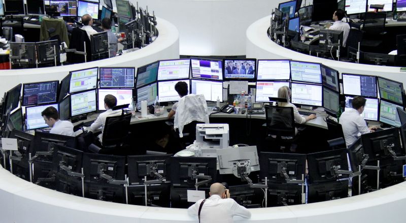FILE PHOTO: Traders work at their desks in front of the German share price index, DAX board, at the stock exchange in Frankfurt