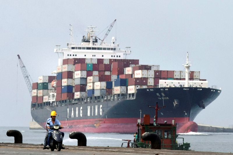 People ride a motorcycle while a container ship passes by at Keelung port in northern Taiwan
