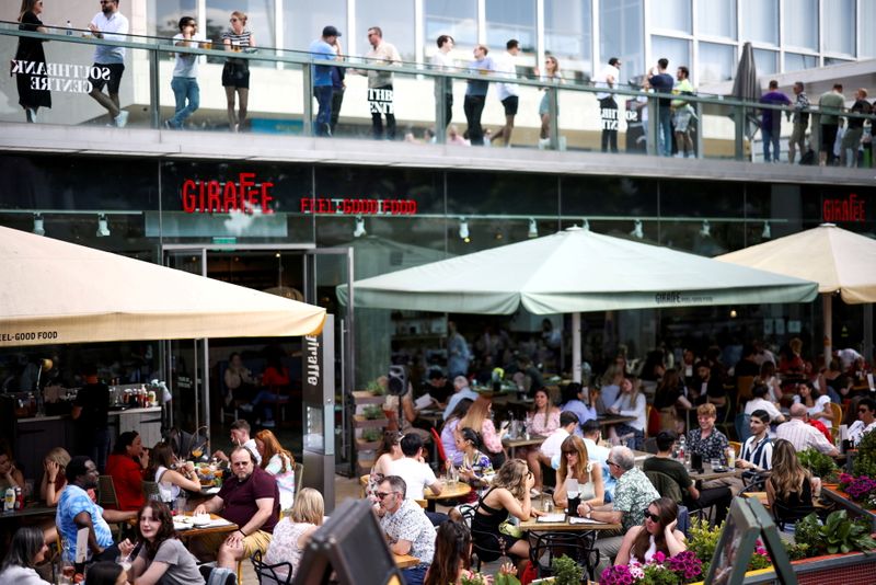 FILE PHOTO: People sit at an outdoor restaurant on the South Bank during sunny weather in London, Britain