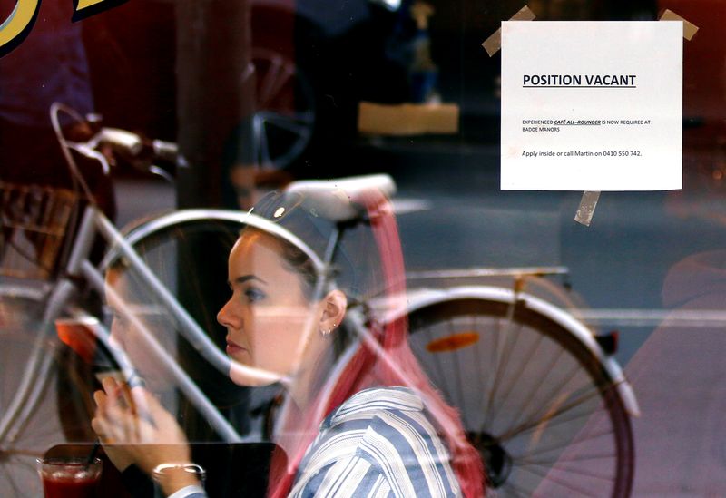 Customers at a local cafe are seen through a window displaying a job vacancy notice in central Sydney, Australia