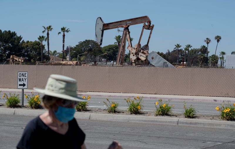 A pedestrian wearing a protective mask walks past an oil derrick in Huntington Beach