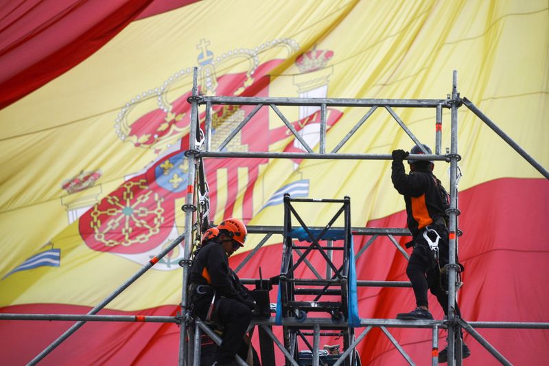 Workers set up a scaffold as a Spanish flag flutters in Madrid