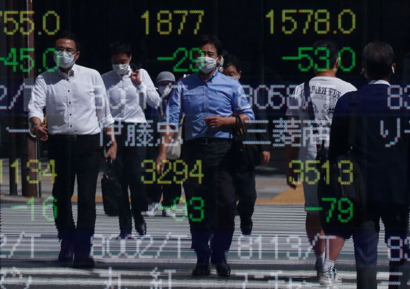 Passersby wearing protective masks are reflected on an electronic board displaying stock prices outside a brokerage amid the COVID-19 outbreak, in Tokyo