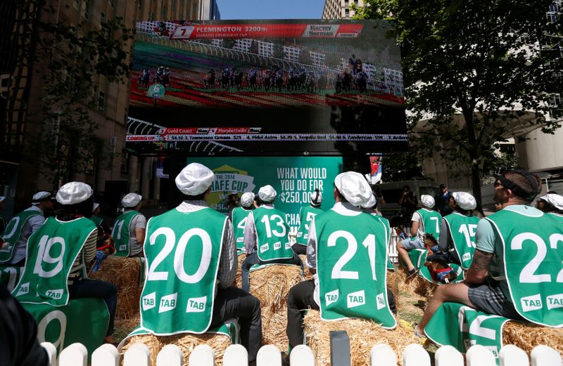 FILE PHOTO: Sports betters sit on 'racehorses' made from hay and toy horse heads as they watch a live telecast of the Melbourne Cup horse race, sponsored by an Australian betting firm in the center of Sydney's business district