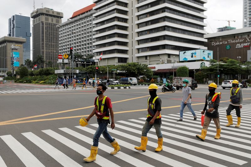 Construction workers wearing protective masks to prevent the spread of the coronavirus disease (COVID-19) cross a main road in Jakarta