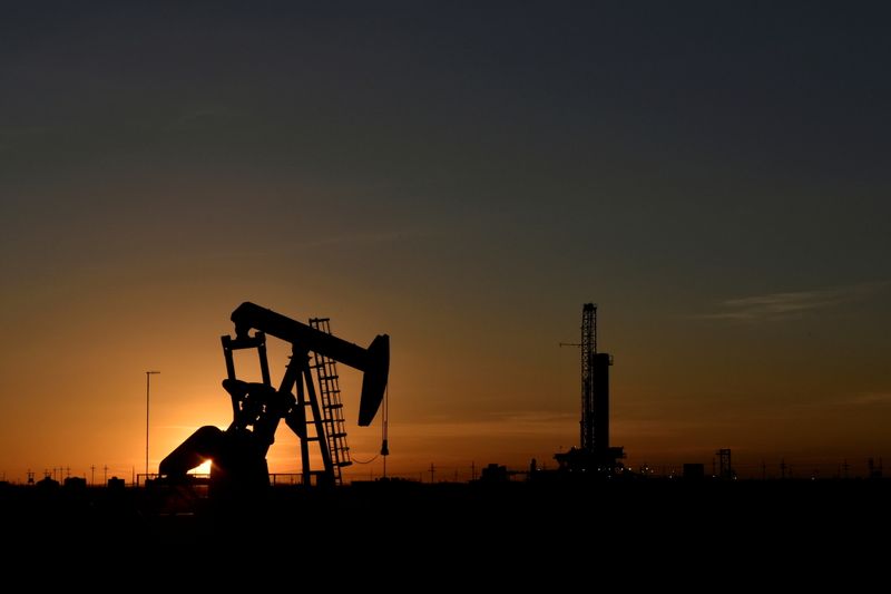 FILE PHOTO: A pump jack operates in front of a drilling rig at sunset in an oil field in Midland, Texas, U.S.