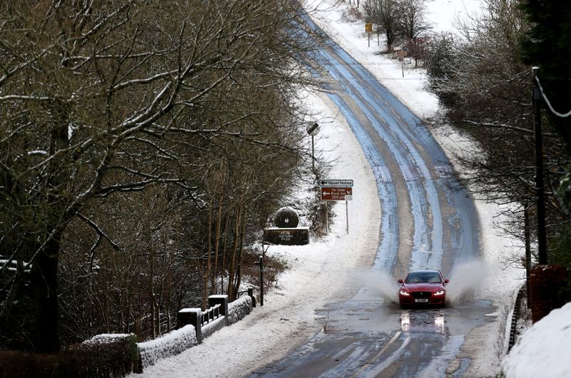 Cars drive along a snow covered flooded road that fell overnight from Storm Arwen, in Leek