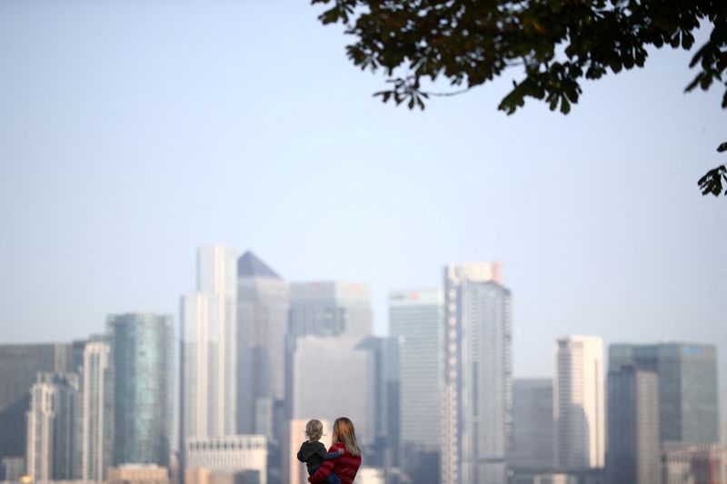 FILE PHOTO: A woman holds a child in front of Canary Wharf skyline, in London