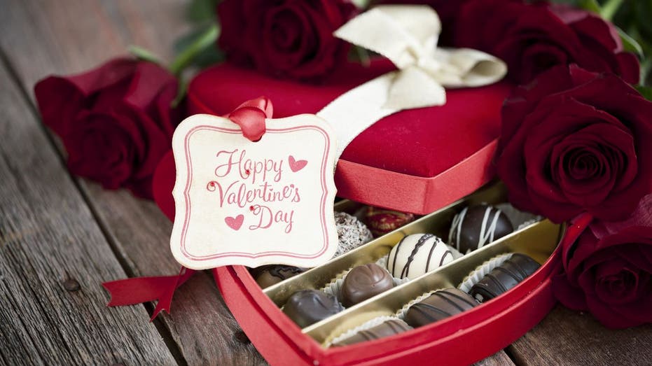 Valentine's Day box of chocolates and red roses on a wood background. 