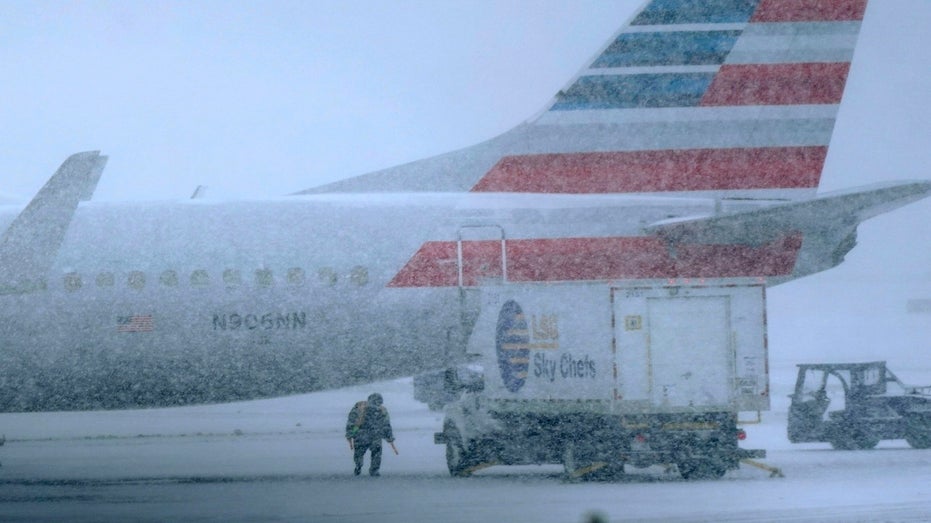 Snow falls on a ground crew working outside a parked plane at Dallas Fort Worth International Airport in Grapevine, Texas, Thursday, Feb. 3, 2022. A major winter storm with millions of Americans in its path is spreading rain, freezing rain and heavy snow further across the country.