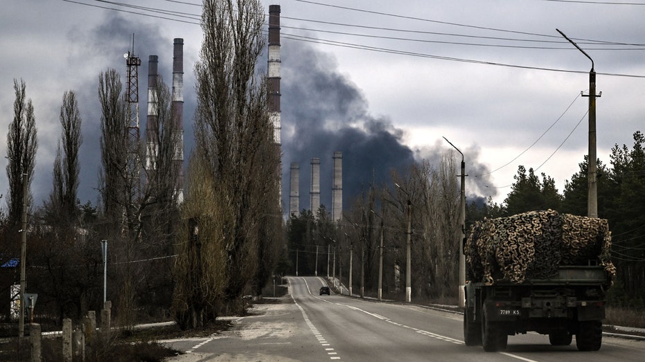 A military vehicle drives on a road as smoke rises from a power plant after shelling outside the town of Schastia, near the eastern Ukraine city of Lugansk, on February 22, 2022, a day after Russia recognised east Ukraine's separatist republics and ordered the Russian army to send troops there as "peacekeepers." 