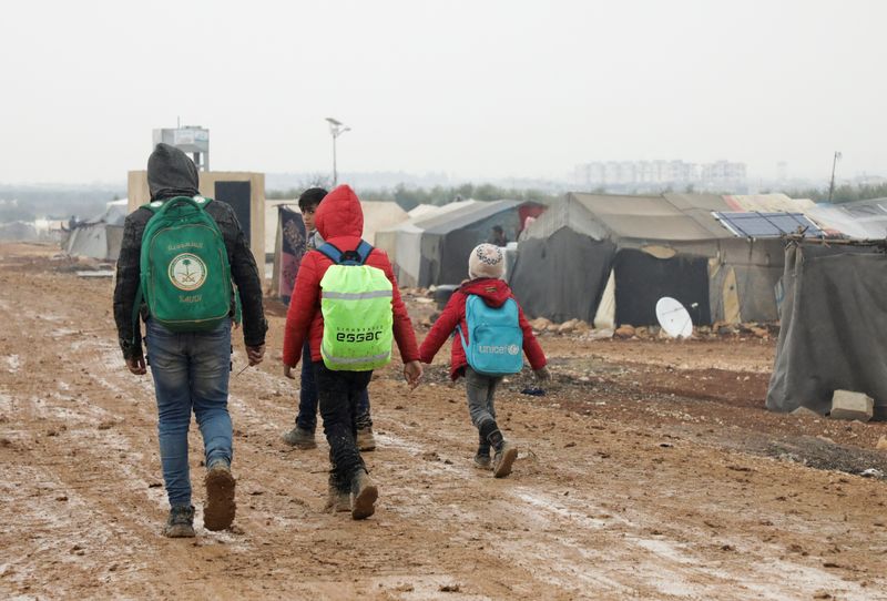 Internally displaced Syrians walk together near tents at a camp in Azaz