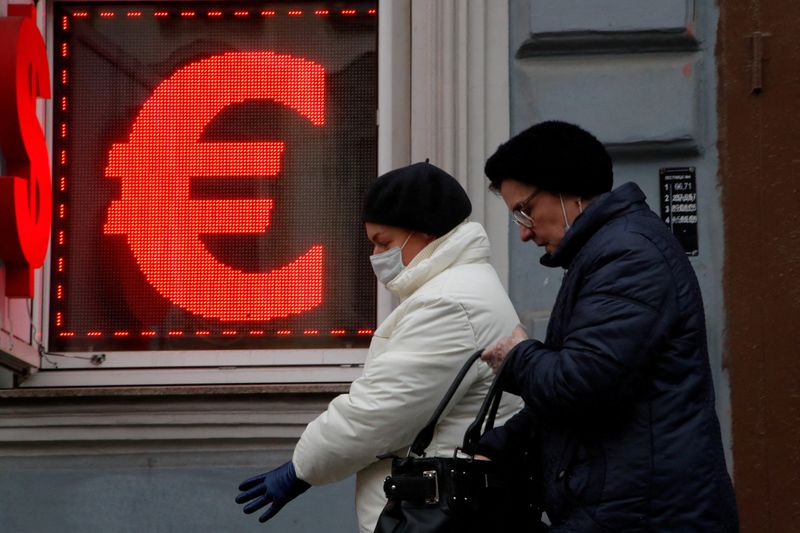 FILE PHOTO: Women walk past a board showing the U.S. dollar and euro signs in Saint Petersburg