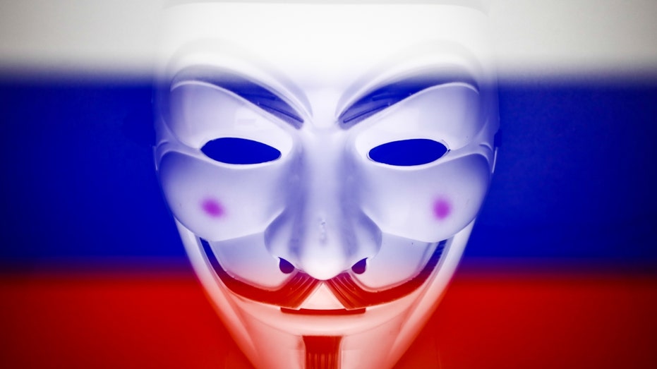 Russian flag displayed on a laptop screen and Guy Fawkes mask are seen in this multiple exposure illustration photo taken in Krakow, Poland on March 1, 2022. Global hacker group Anonymous declared 'cyber war' against Russia. (Photo by Jakub Porzycki/NurPhoto via Getty Images)