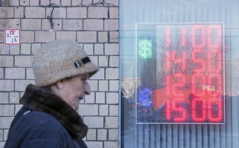 A woman walks past a board showing currency exchange rates of the Euro and the U.S. dollar against the Russian rouble in Moscow