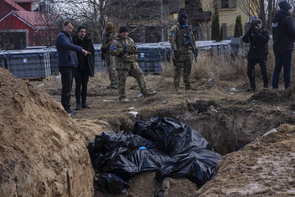 People stand next to a mass grave in Bucha, on the outskirts of Kyiv, Ukraine, Monday, April 4, 2022. Russia is facing a fresh wave of condemnation after evidence emerged of what appeared to be deliberate killings of dozens if not hundreds of civilians in Ukraine. (AP Photo/Rodrigo Abd)
