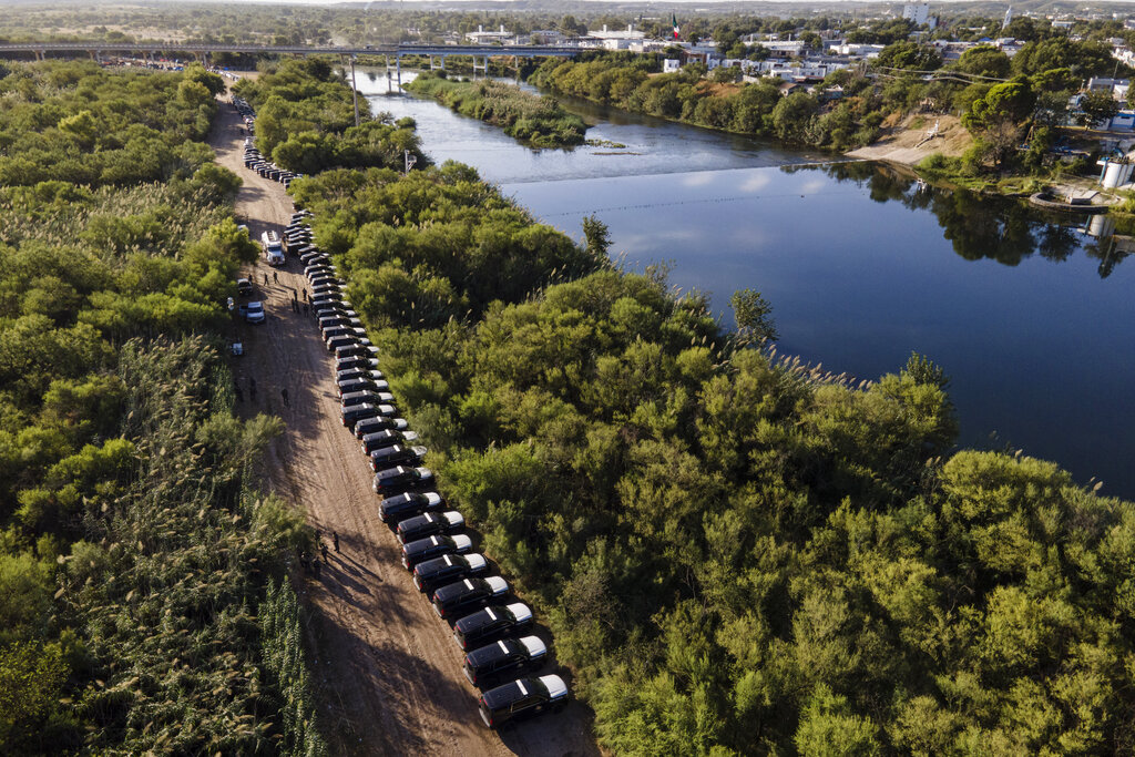 FILE - A line of Texas Department of Safety vehicles line up on the Texas side of the Rio Grande with Mexico visible, right, near an encampment of migrants, many from Haiti, on Sept. 22, 2021, in Del Rio, Texas. Former Trump administration officials are pressing Republican border governors to declare an "invasion" along the U.S.-Mexico border. It comes as Texas Gov. Greg Abbott says he'll announce "unprecedented actions" on Wednesday to deter migrants coming to Texas. (AP Photo/Julio Cortez, File)