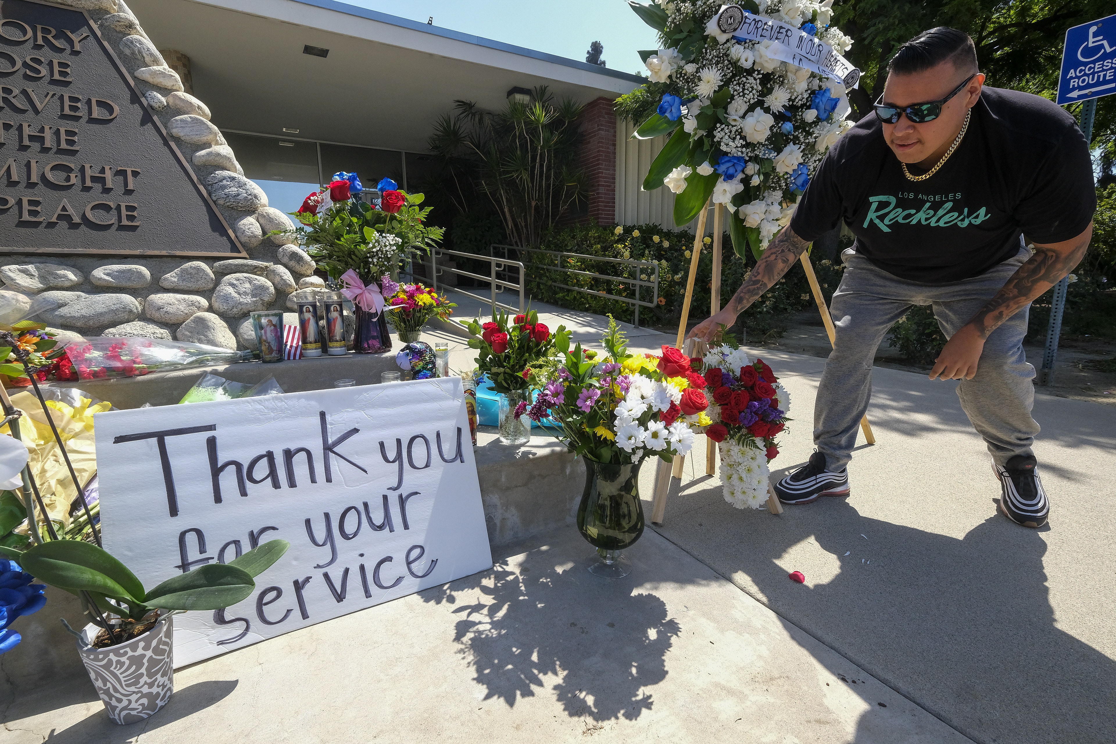 A man places flowers at a memorial Wednesday, June 15, 2022, outside El Monte City Hall for two police officers who were shot and killed Tuesday, at a motel in El Monte, Calif. The two police officers were killed in a shootout while investigating a possible stabbing in the suburban Los Angeles motel, and the suspect died at the scene, authorities said. (AP Photo/Ringo H.W. Chiu)