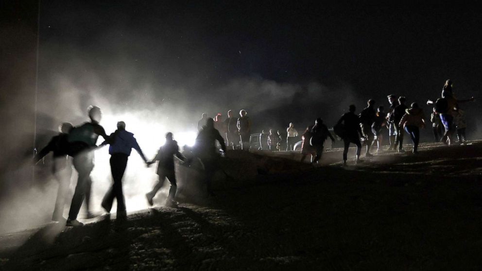 PHOTO: Immigrants cross through a gap in the U.S.-Mexico border barrier as others watch from above before being processed by the U.S. Border Patrol in Yuma, Ariz., May 23, 2022.