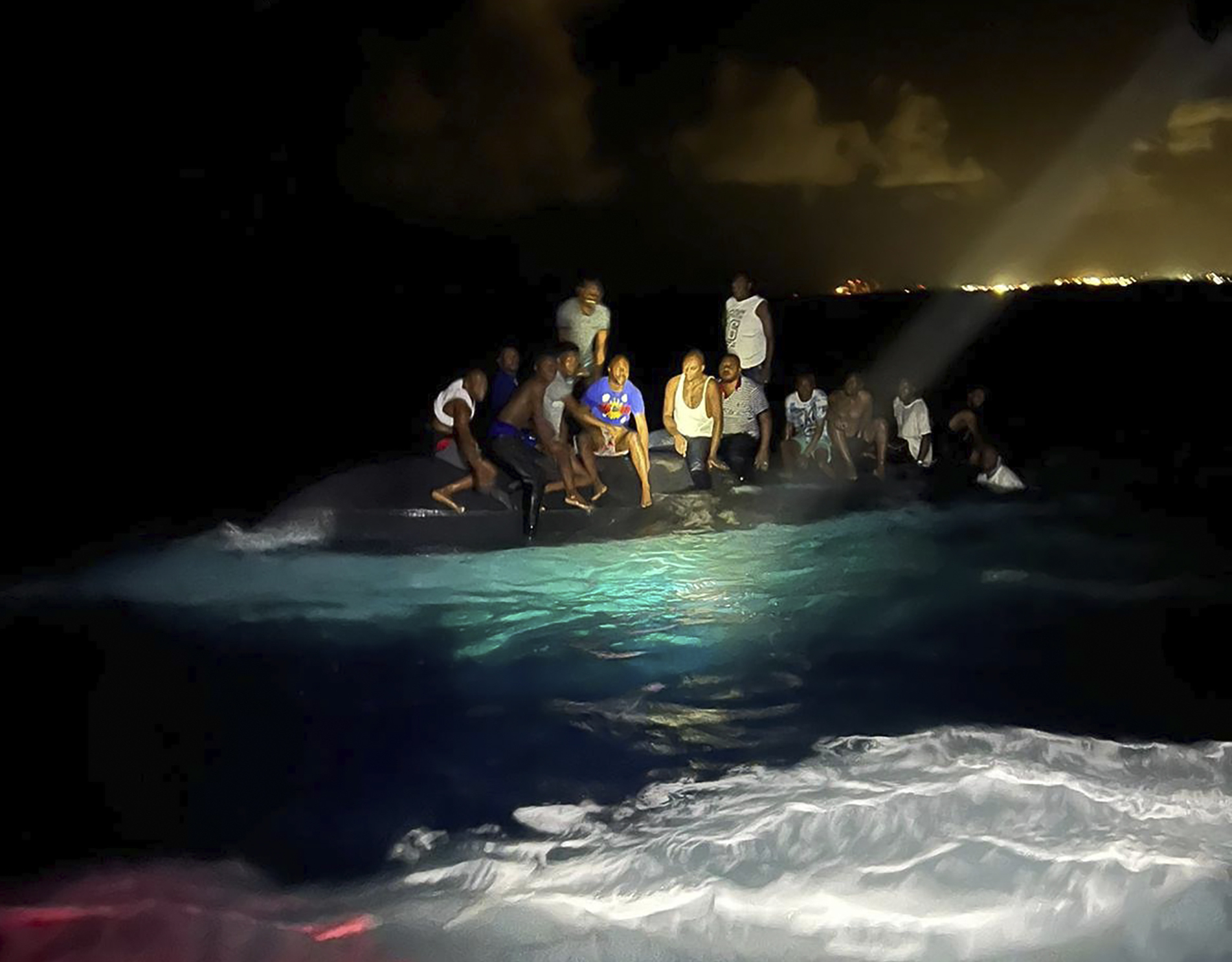 In this photo provided by the Royal Bahamas Defense Force, survivors sit on a capsized boat as they are about to be rescued near New Providence in the Bahamas, early Sunday, July 24, 2022. Bahamas Prime Minister Philip Brave Davis said in a statement that the dead included 15 women, one man and an infant. (Royal Bahamas Defense Force via AP)