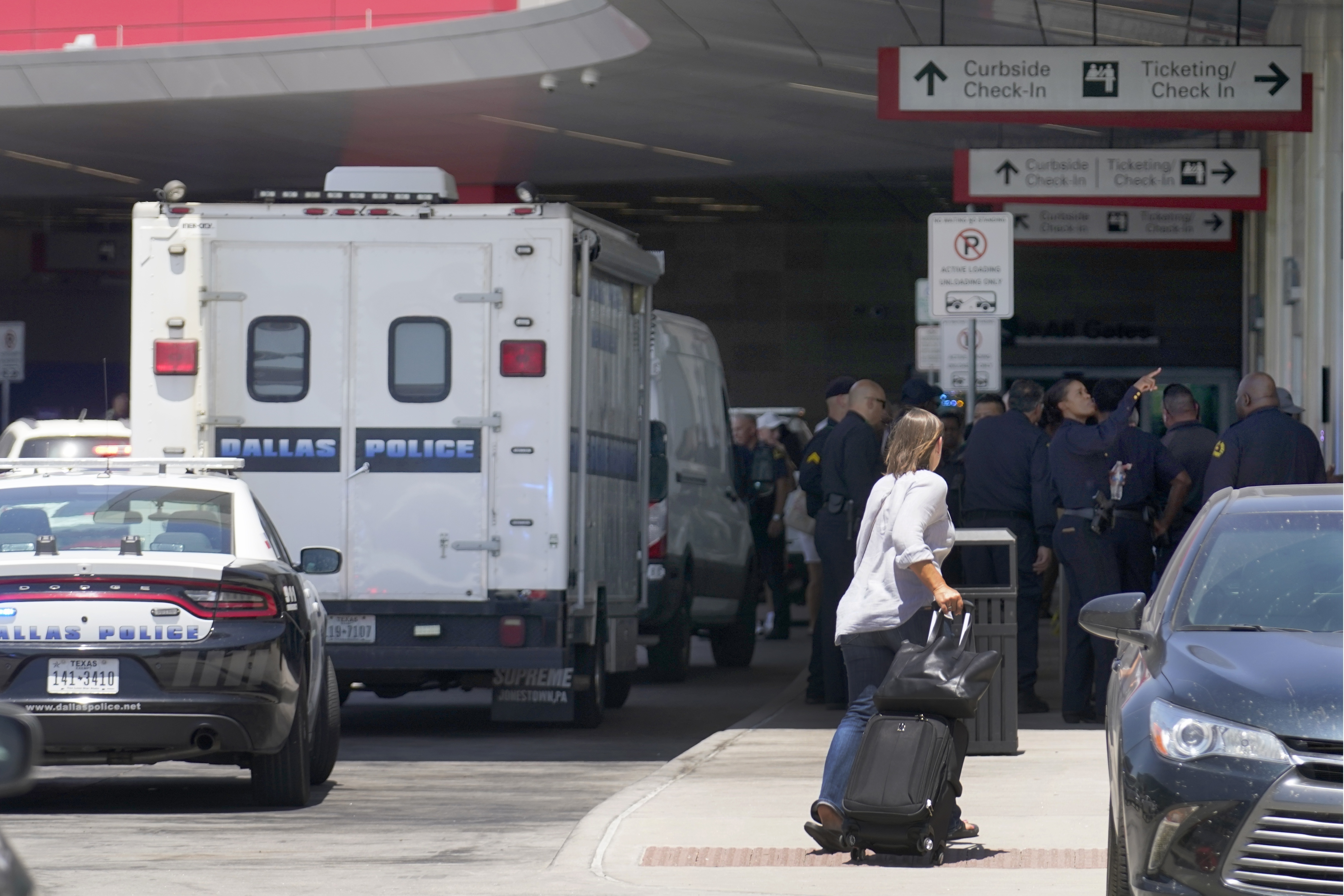 A traveler makes her way past emergency responders standing outside the ticketing and check in area at Dallas Love Field in Dallas, Monday, July 25, 2022. A 37-year-old woman fired several gunshots, apparently at the ceiling, inside of Dallas' Love Field Airport on Monday before an officer shot and wounded her, authorities said. (AP Photo/Tony Gutierrez)