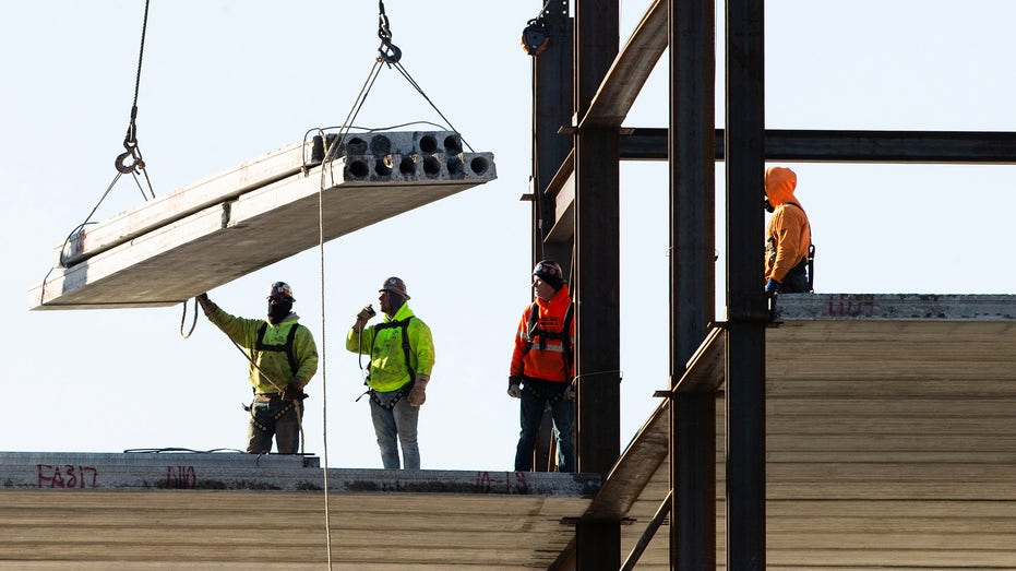 Workers lift steel beams at construction site