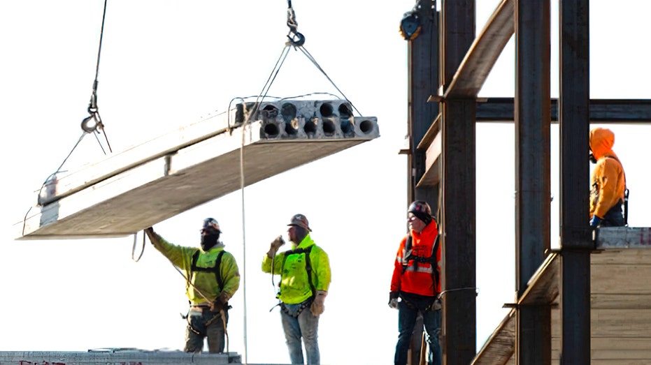 Workers are seen adding material to a building that is under construction