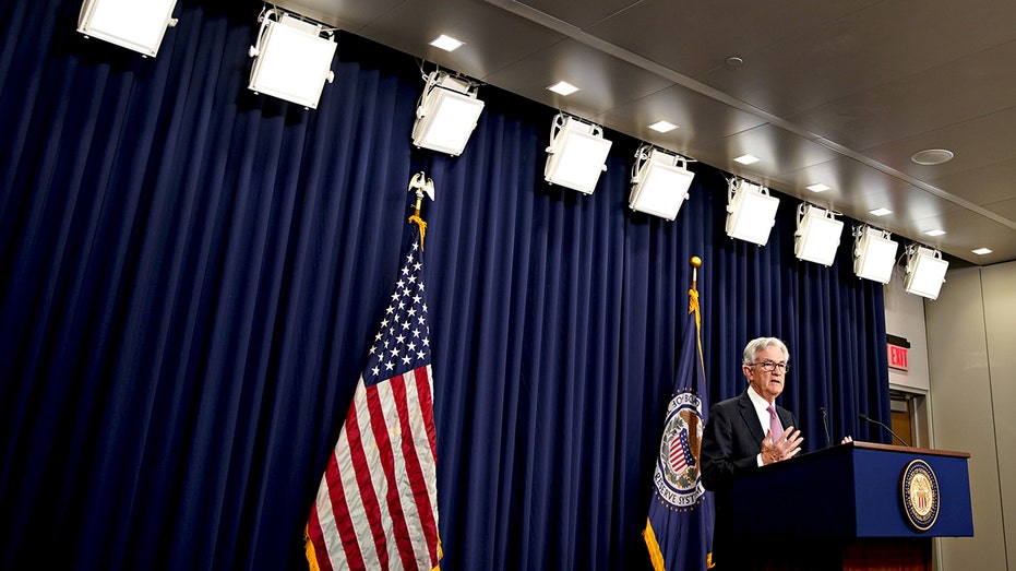 Jerome Powell speaks in front of a podium with flags in the background