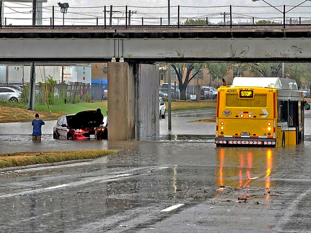 PHOTO: People stand next to a vehicle sitting in flood waters, along a street in Dallas, on Aug. 22, 2022, in a handout photo provided by the Dallas Police Depart. Heavy rains were causing havoc in parts of Texas.