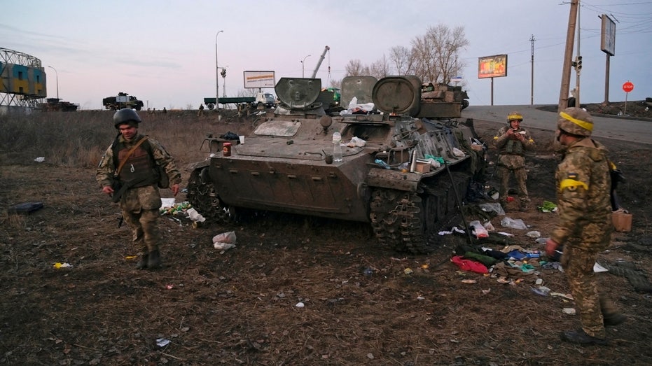 Ukrainian servicemen are seen next to a destroyed armoured vehicle, which they said belongs to the Russian army, outside Kharkiv