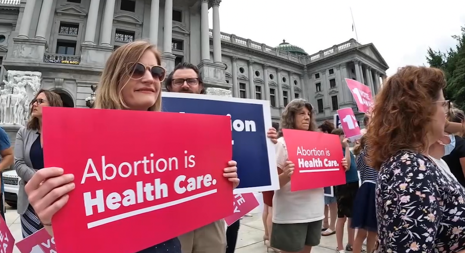 Protesters holding signs in front of the Pennsylvania State capitol. One sign reads 'Abortion is Health Care.' 