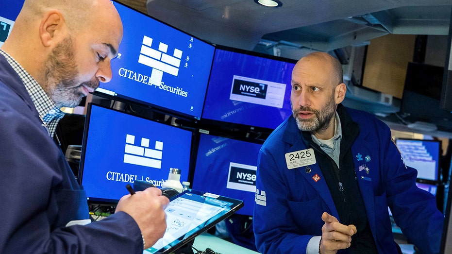 Two men wearing blue jackets on the floor of the New York Stock Exchange