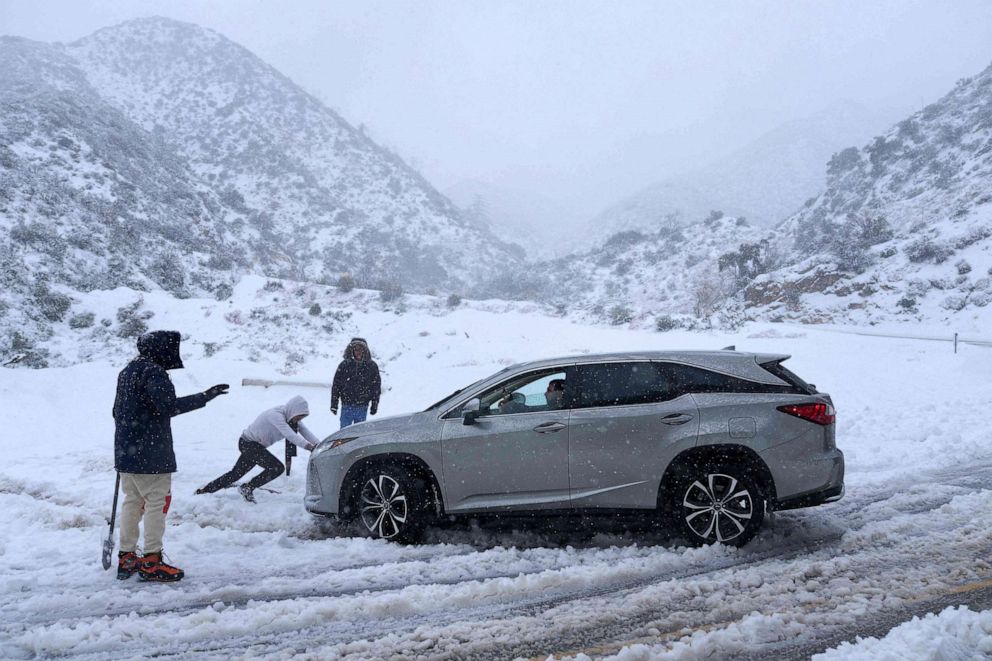 PHOTO: A person helps push out a vehicle that became stuck in the snow on a roadway in the San Gabriel Mountains in the Angeles National Forest, Calif., on Feb. 24, 2023.