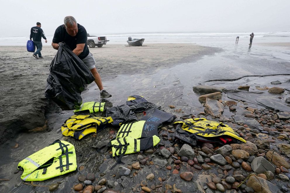 PHOTO: Boat salvager Robert Butler, front, picks up life preservers in front of one of two boats sitting on Blacks Beach, March 12, 2023, in San Diego.