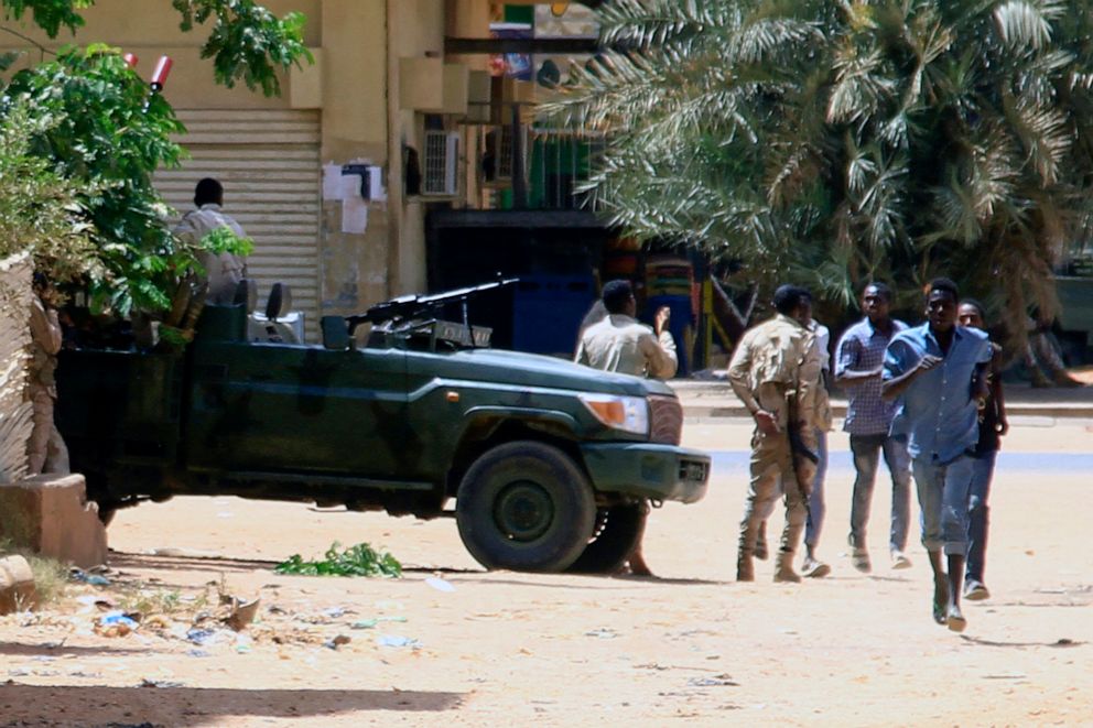 PHOTO: People run past a military vehicle in Khartoum, Sudan, on April 15, 2023, amid reported clashes in the city.