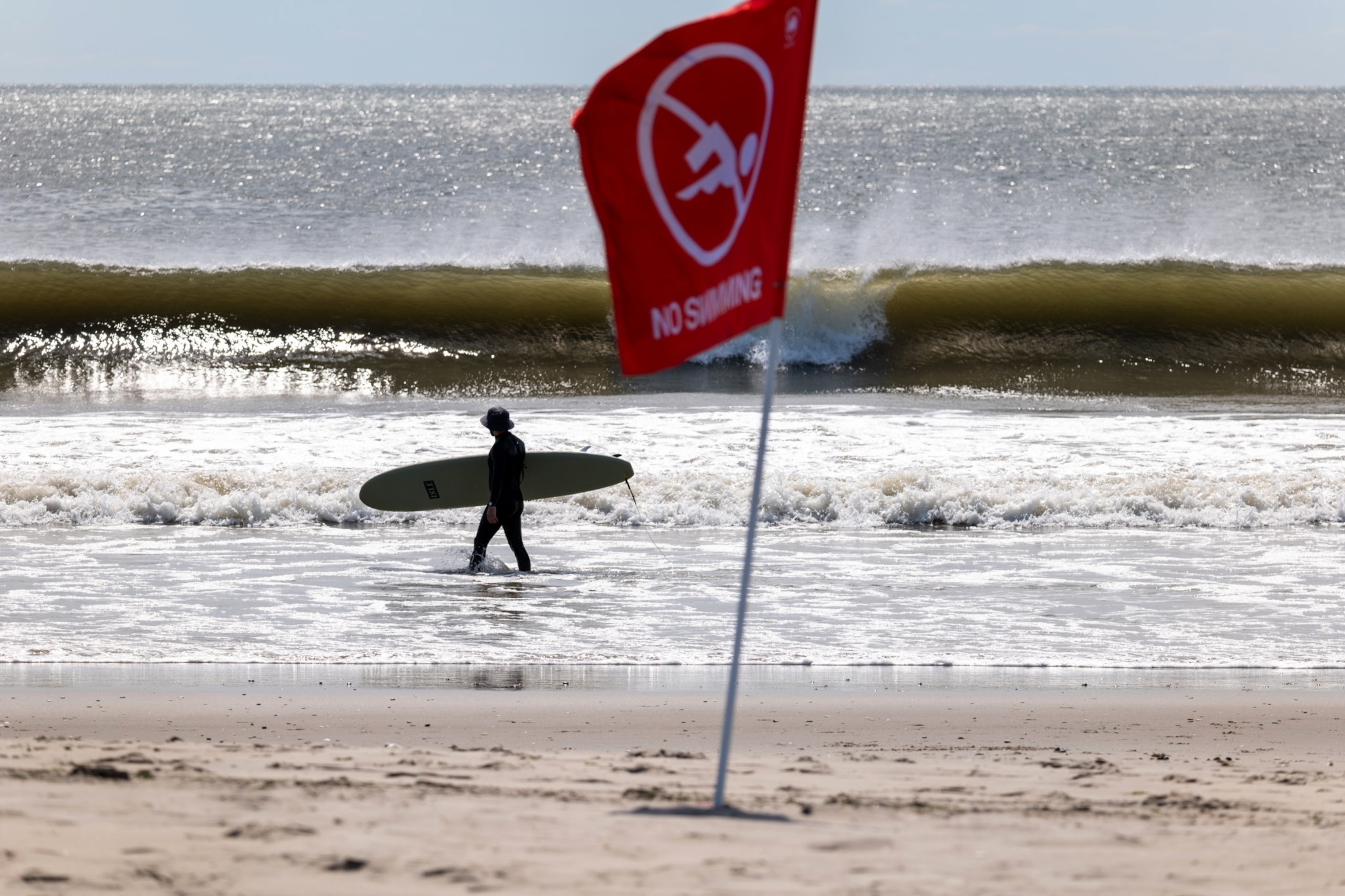 PHOTO: A surfer walks along Rockaway Beach in New York as high surf from Hurricane Franklin delivers strong rip tides and large waves to most of the eastern seaboard on August 31, 2023 in New York City.