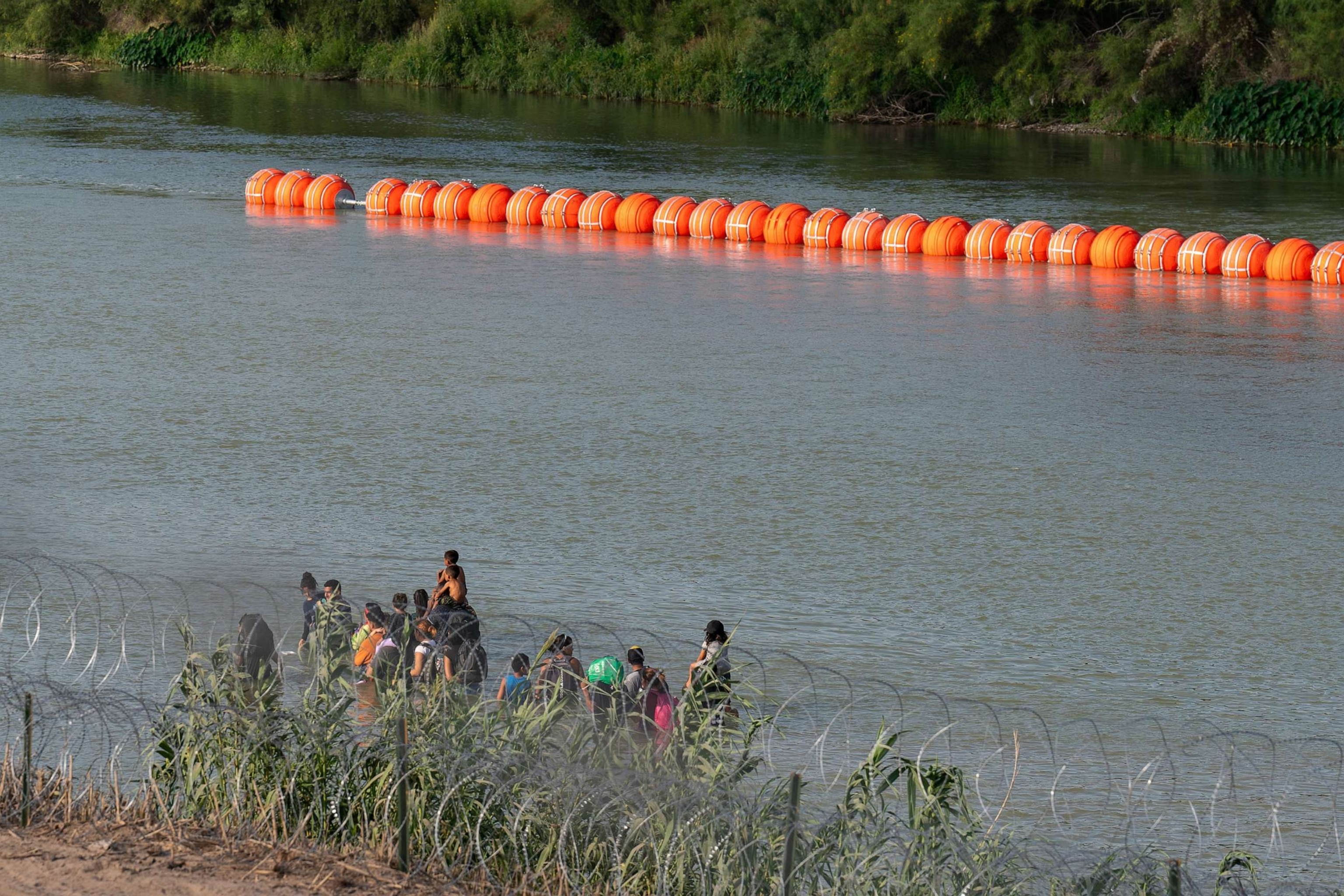 PHOTO: In this July 16, 2023, file photo, migrants walk by a string of buoys placed on the water along the Rio Grande border with Mexico, in Eagle Pass, Texas.