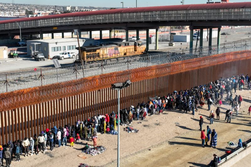 CIUDAD JUAREZ, MEXICO - DECEMBER 21: As seen from an aerial view, migrants line up along the U.S. Mexico border fence to apply for asylum in the United States on December 21, 2022 as viewed from Ciudad Juarez, Mexico. Texas Governor Greg Abbott ordered 400 troops to the U.S.-Mexico border in El Paso, which is under a state of emergency due to a surge of migrants crossing from Mexico into the city. Border officials expect an even larger migrant surge at the border if the pandemic era Title 42 regulation is lifted. (Photo by John Moore/Getty Images)