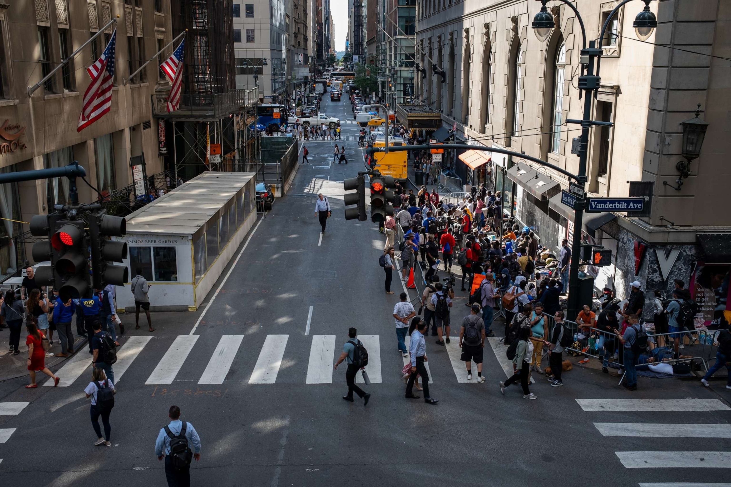 PHOTO: People walk past migrants gathered outside of the Roosevelt Hotel where dozens of recently arrived migrants have been camping out as they try to secure temporary housing, Aug. 2, 2023, in New York.