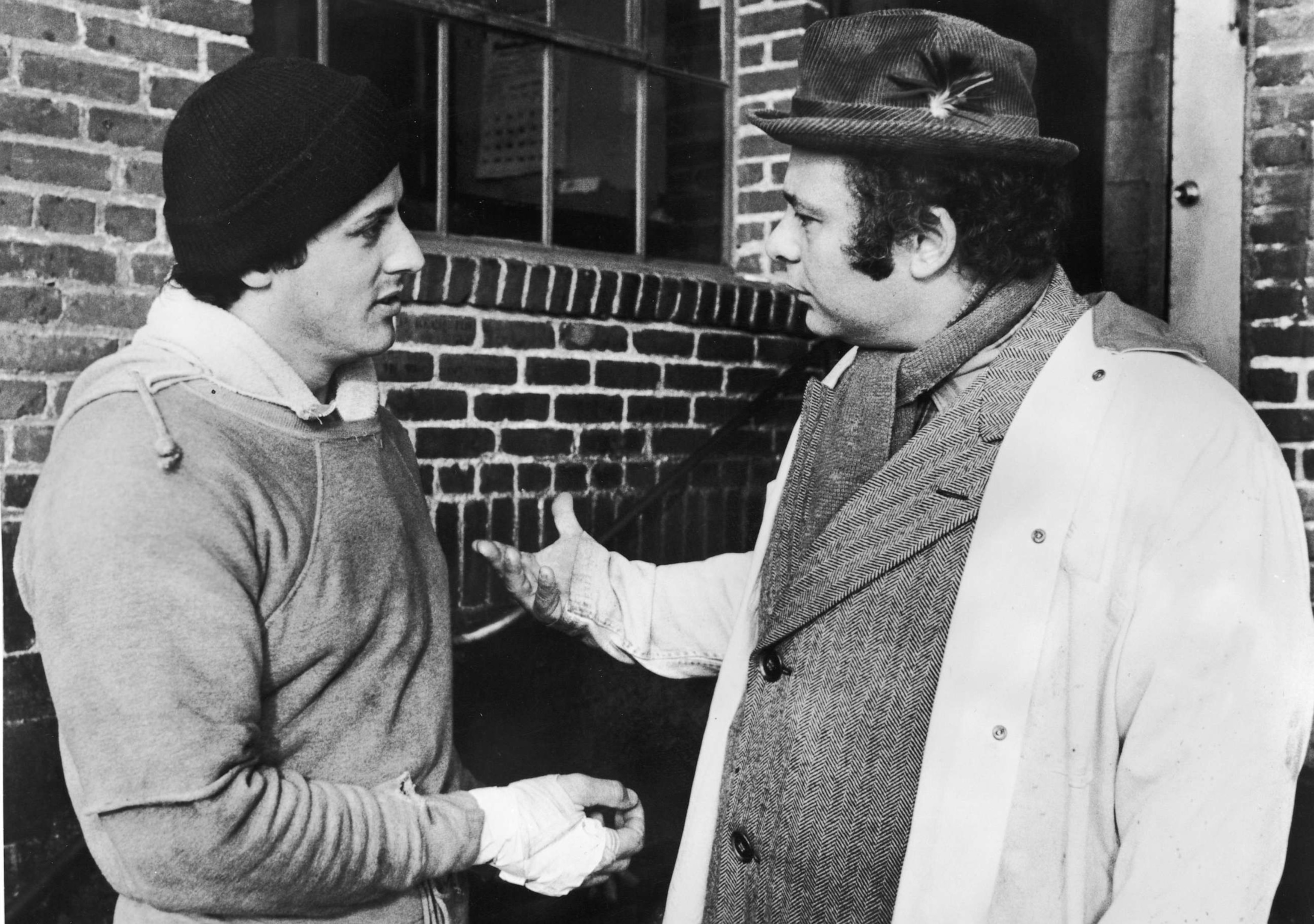 PHOTO: American actors Sylvester Stallone (L), wearing training clothes, and Burt Young talk outdoors in a still from the film, 'Rocky,' directed by John G. Avildsen, 1976. (Photo by United Artists/Courtesy of Getty Images)