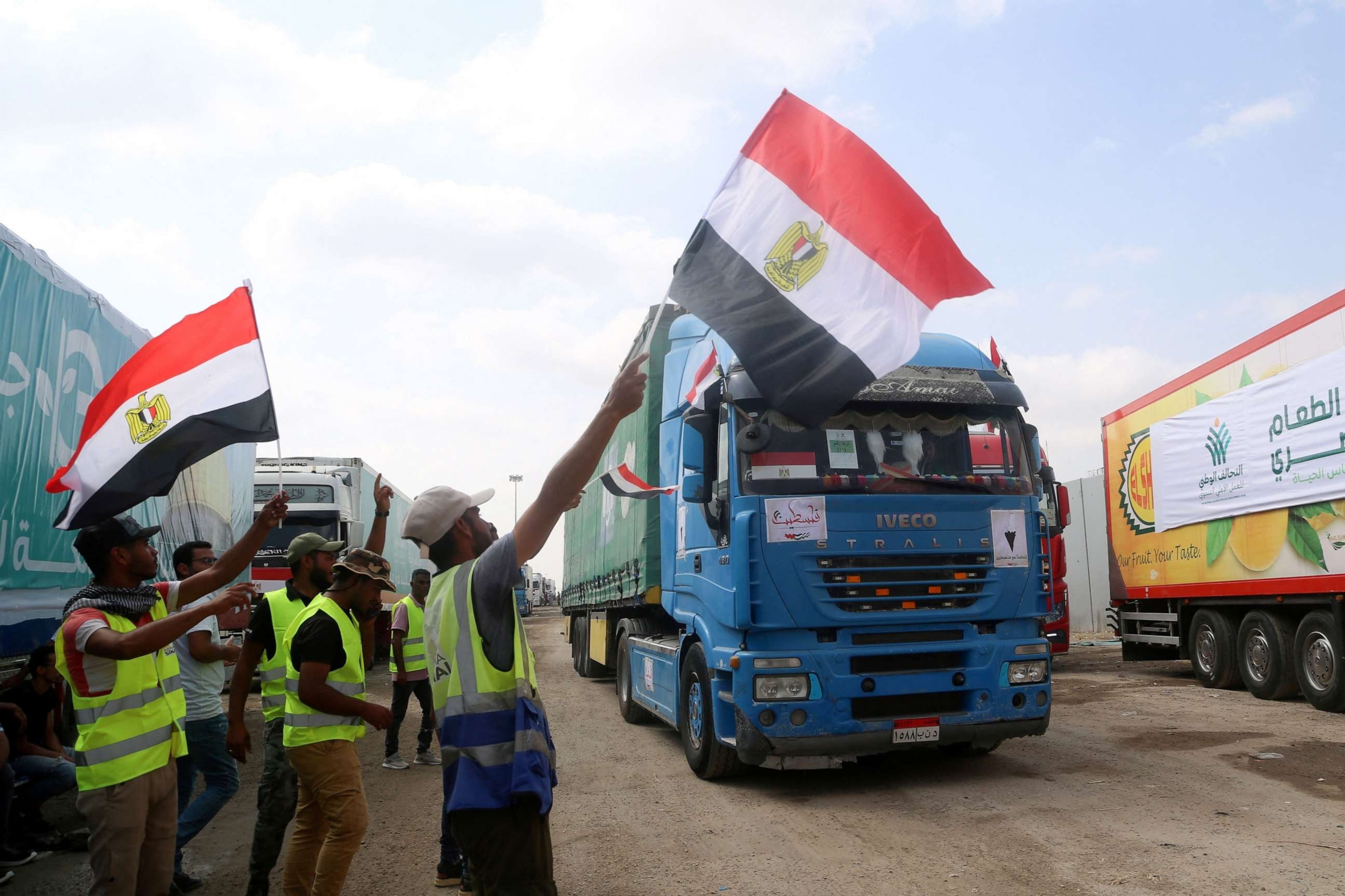 PHOTO: People on the Egyptian side of the Rafah border crossing wave flags as a convoy of lorries carrying humanitarian aid crosses to the Gaza Strip on Oct. 22, 2023.