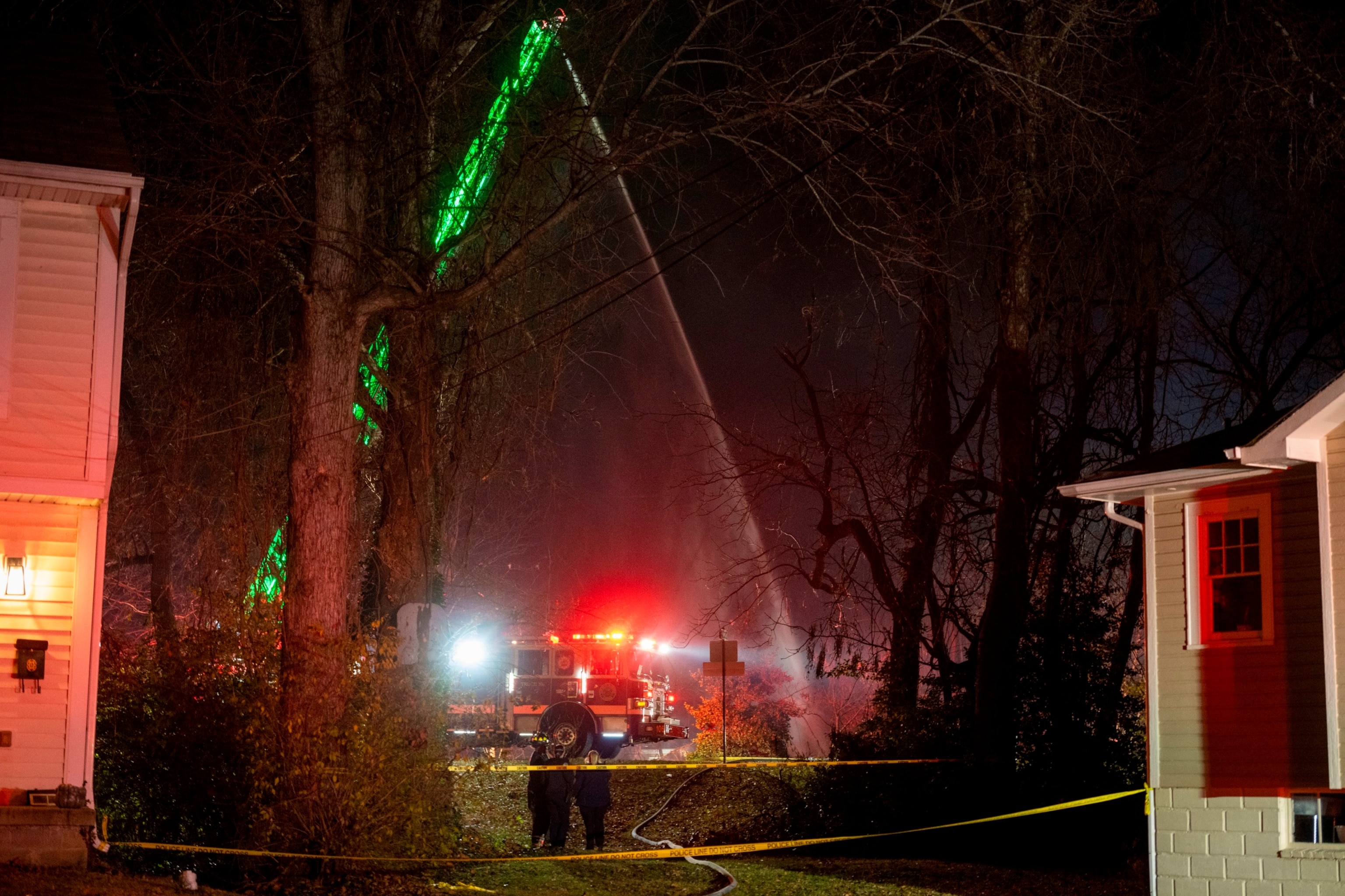 PHOTO: Fire and police officials walk around the scene of a house explosion as an Arlington County Fire Department ladder truck sprays water down on the remains of the building on Monday, Dec. 4, 2023, in Arlington, Va. 