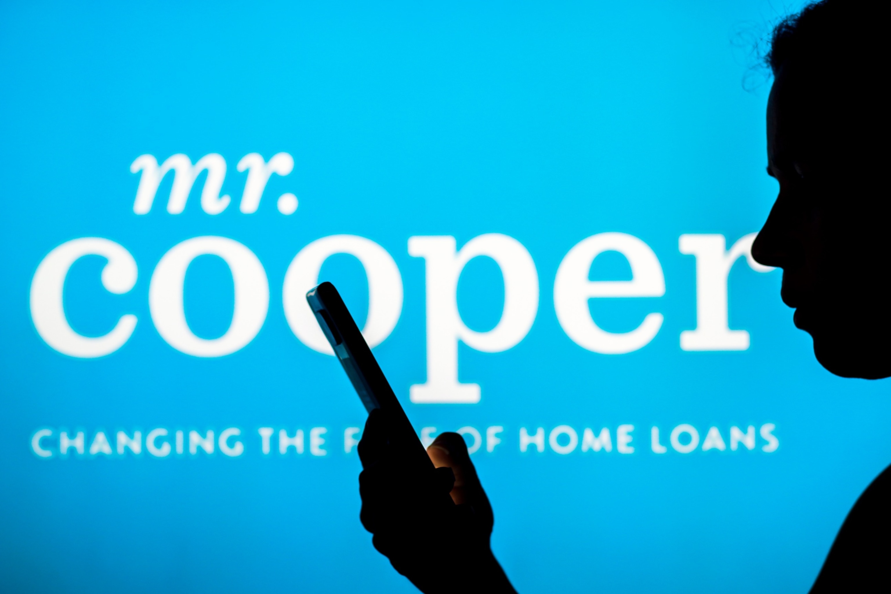 PHOTO: The Mr. Cooper logo is seen in the background of a silhouetted person holding a mobile phone.