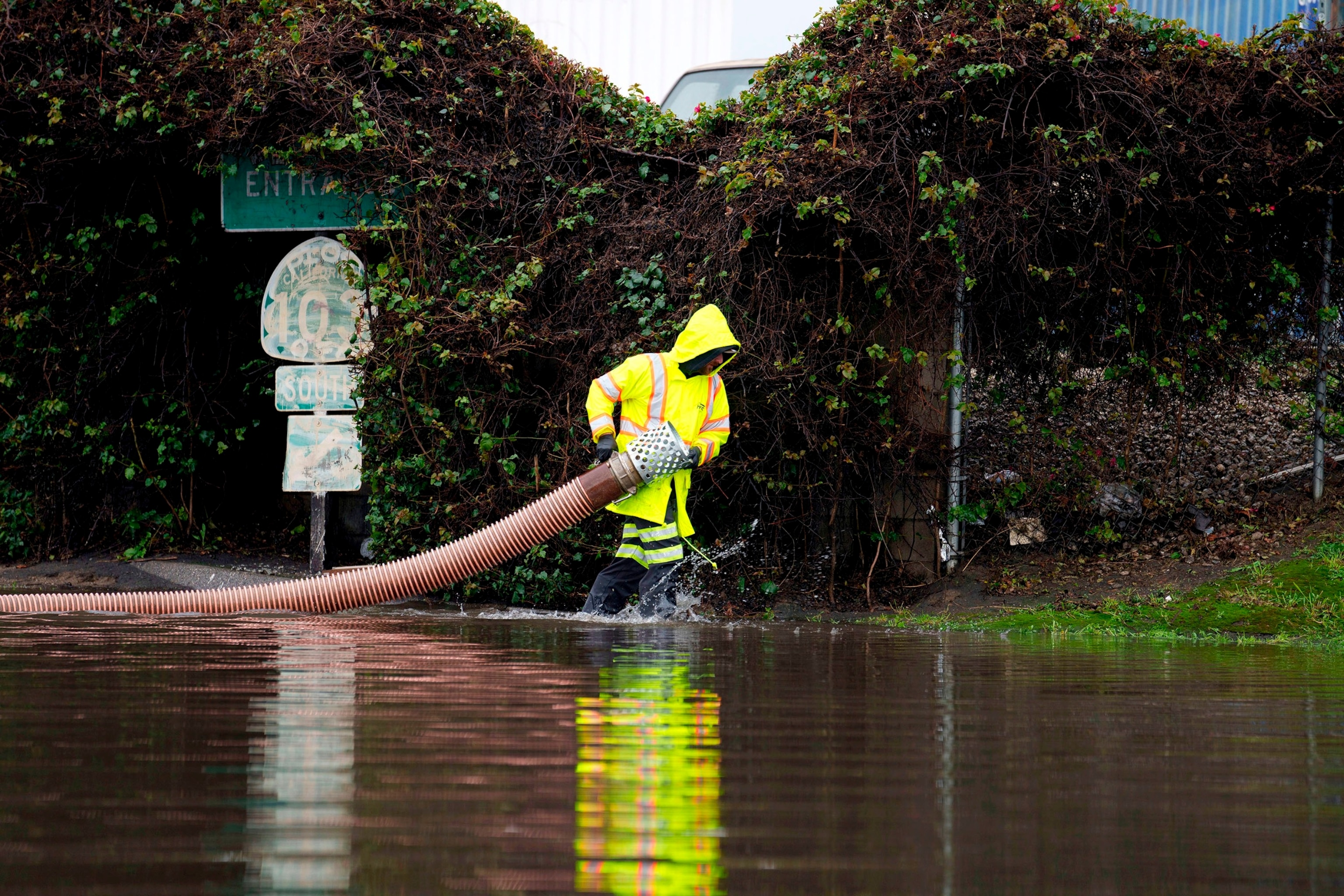 PHOTO: A worker carries a hose on a flooded street, on Feb. 1, 2024, in Long Beach, Calif. 