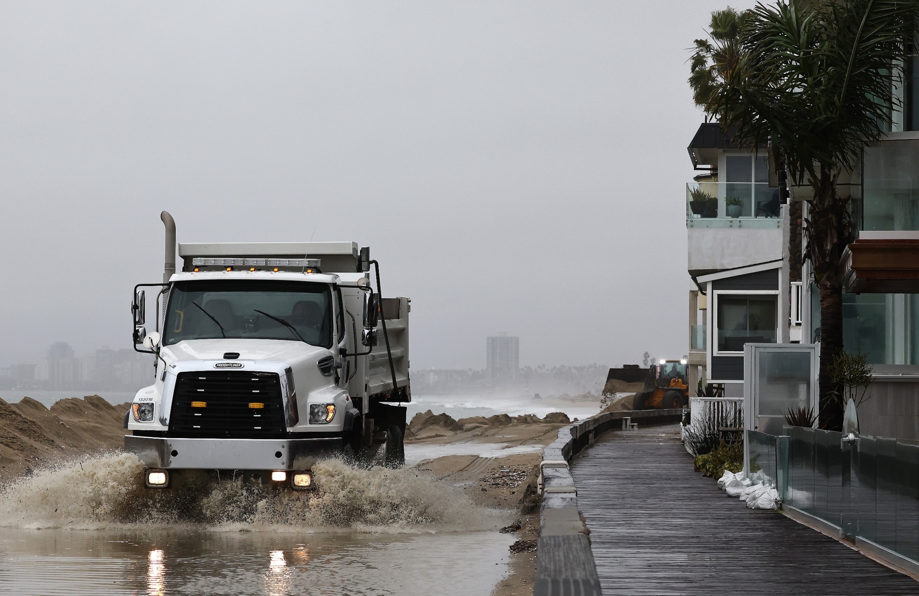 PHOTO: A worker drives through standing water while creating sand berms to protect beachfront homes from flooding, Feb. 20, 2024, in Long Beach, Calif.