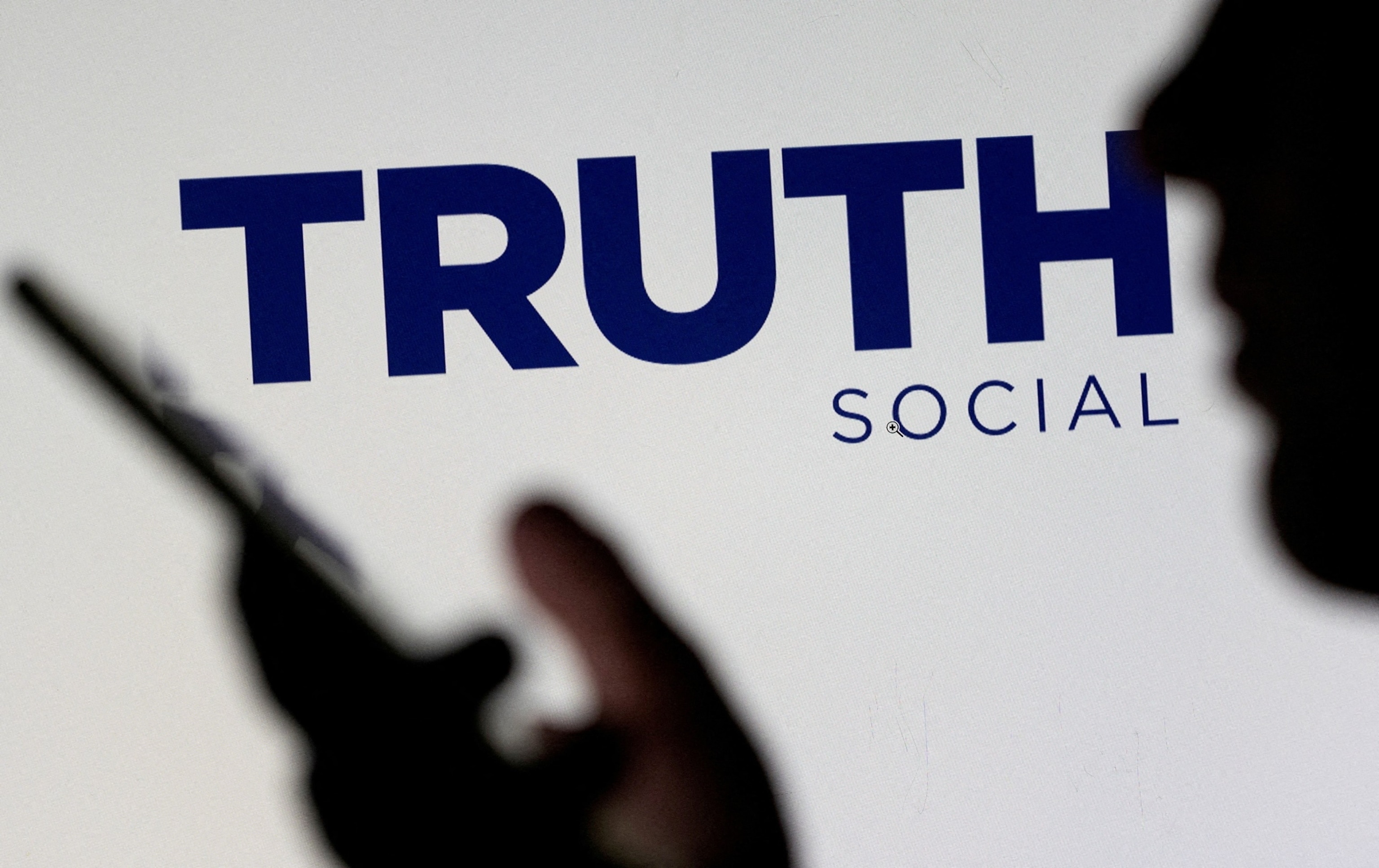 PHOTO: The Truth social network logo is seen displayed behind a woman holding a smartphone in this picture illustration, Feb. 21, 2022. 